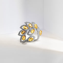 A sculptural silver ring featuring a leaf-like cluster of pear-cut yellow gemstones and pavé-set clear stones, photographed on a clean white surface.