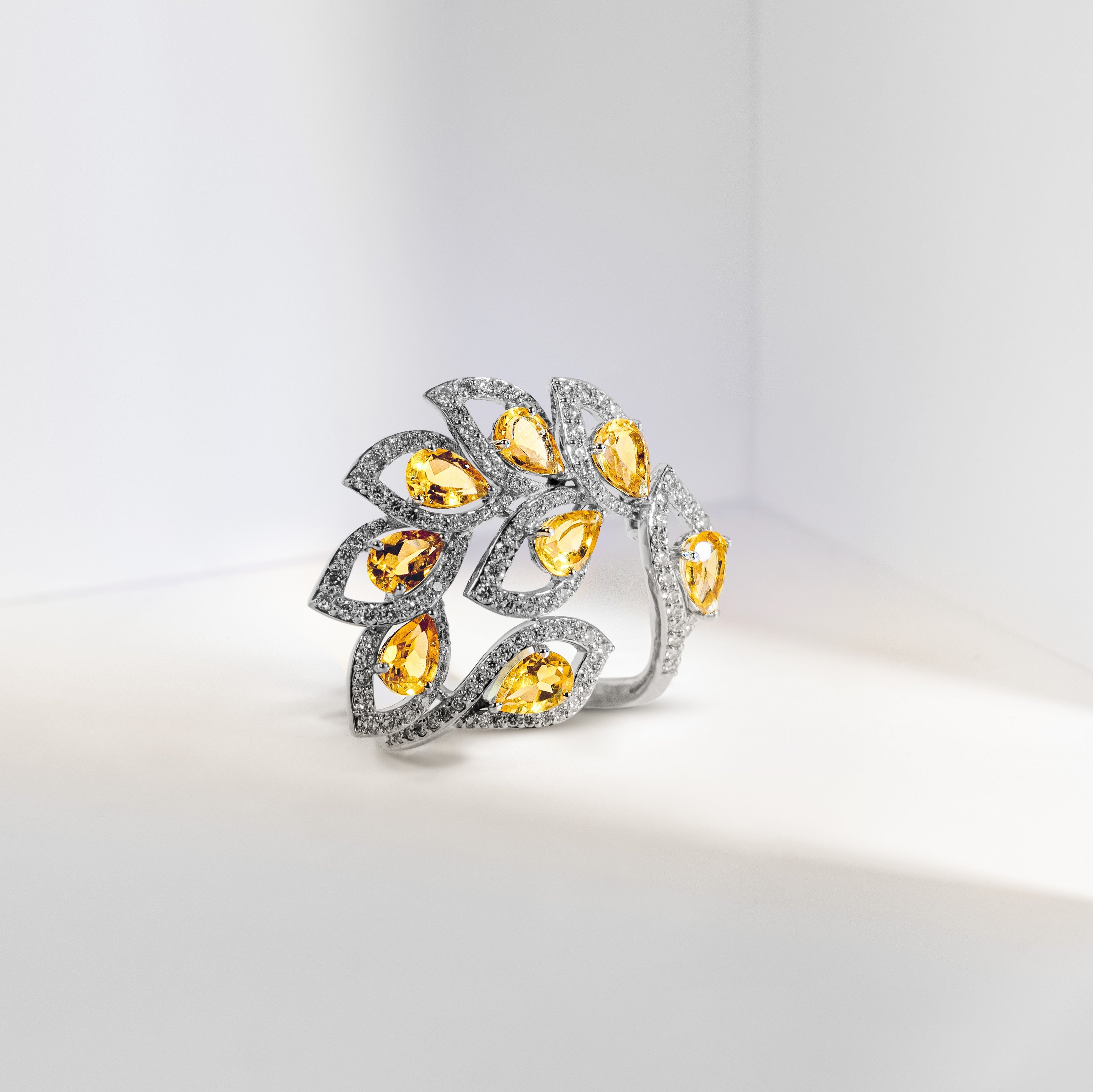 A sculptural silver ring featuring a leaf-like cluster of pear-cut yellow gemstones and pavé-set clear stones, photographed on a clean white surface.