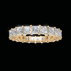 A yellow gold eternity ring featuring a row of baguette-cut clear gemstones, shown against a solid black background.